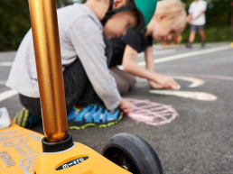 Zwei Kinder malen mit Straßenkreide ein Bild